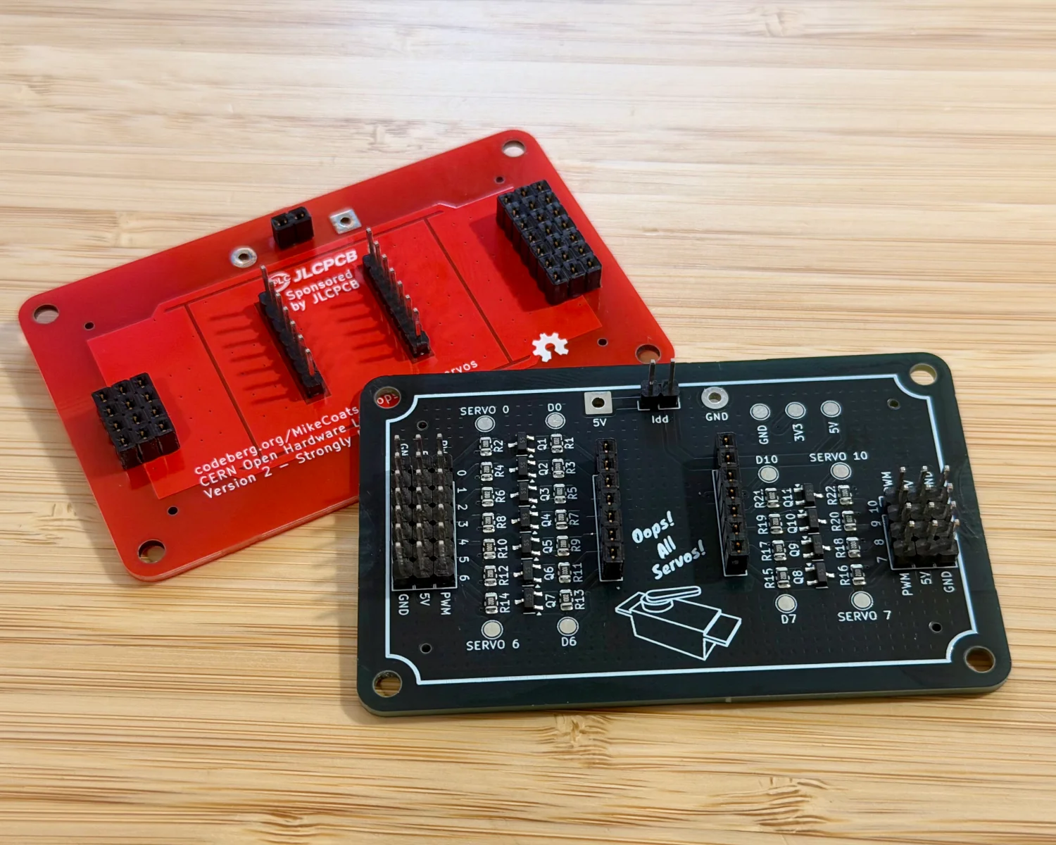A red PCB, configured as a build jig, and a black PCB configured as a full "Oops! All Servos!" Board.