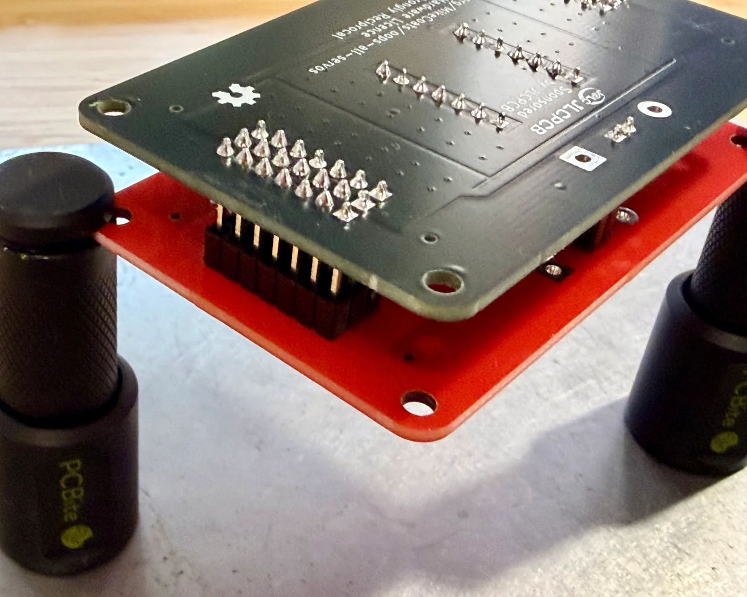 The red and black PCBs during assembly. The red jig is holding the black PCBs components in place for soldering.