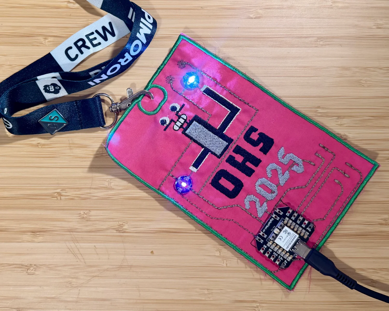 A photgraph of my OHS2025 badge with two NeoPixels illuminated.